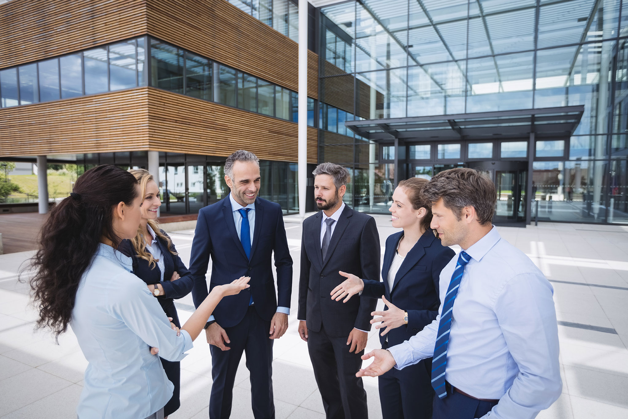 A diverse group of business professionals engaged in conversation outside a modern office building, symbolizing collaboration and synergy. This image depicts AZEE Training team development activities