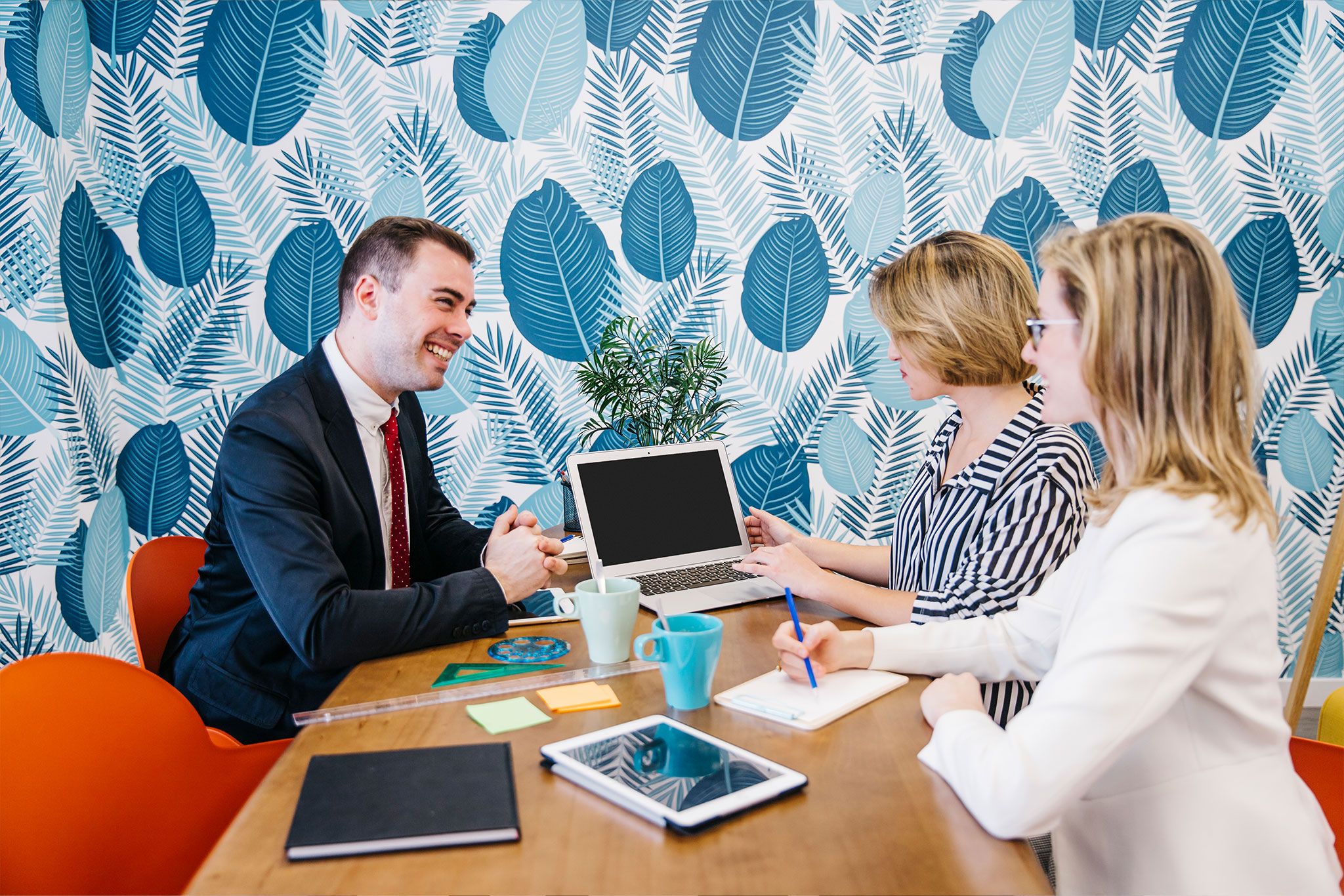 Three professionals, collaborating around a laptop in a meeting, representing AZEE Training course on Business Communication.