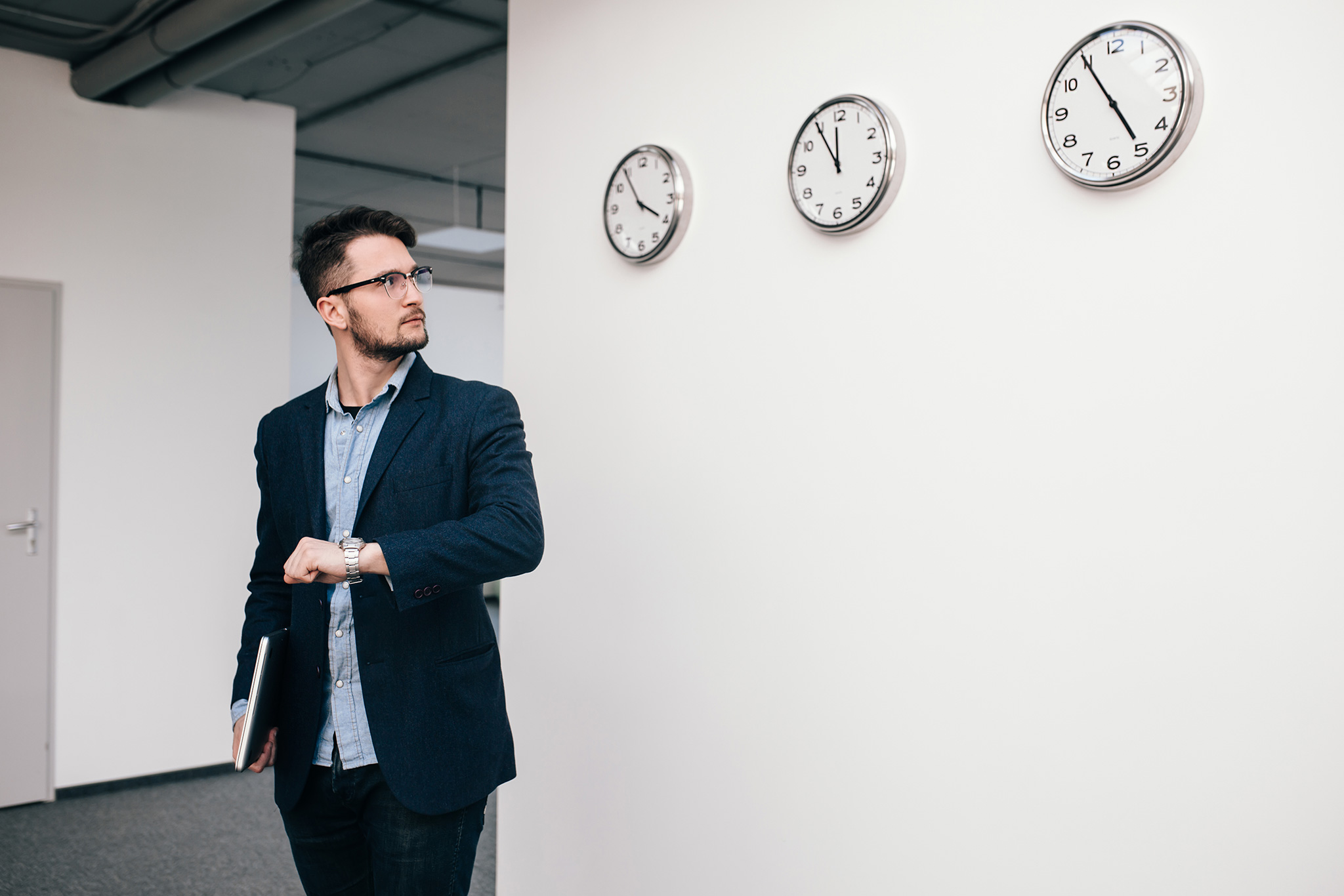 A man checking his watch near clocks on a wall, depicting the importance of efficiency. This image supports AZEE Training time management course for Productivity and Focus.